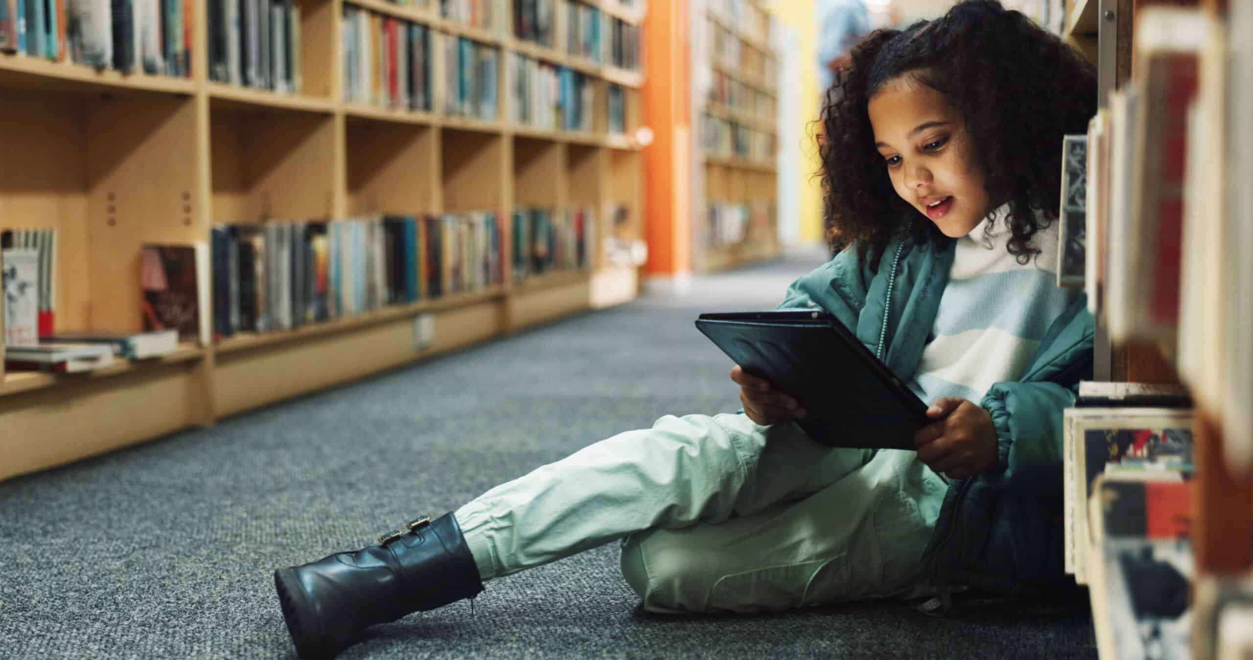 Young girl reading on a tablet while sitting in a library