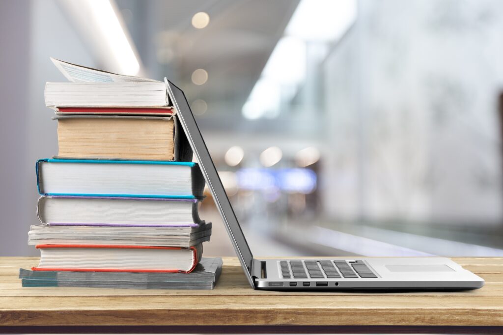 Side profile of a stack of books leaning against an open laptop